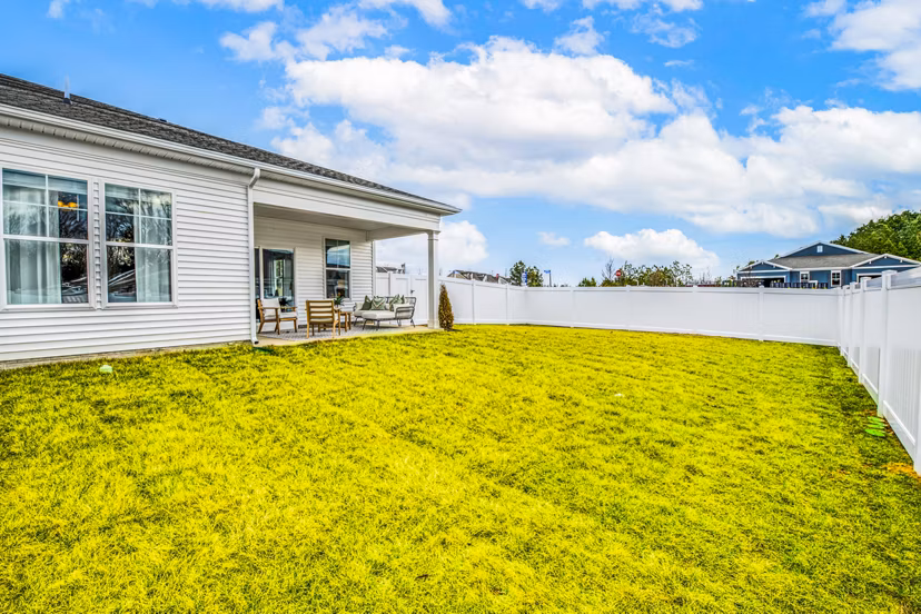 Backyard with grassy lawn, white fence, and covered patio with outdoor seating at luxury apartments