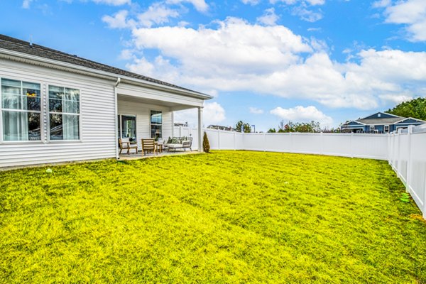 Backyard with grassy lawn, white fence, and covered patio with outdoor seating at luxury apartments