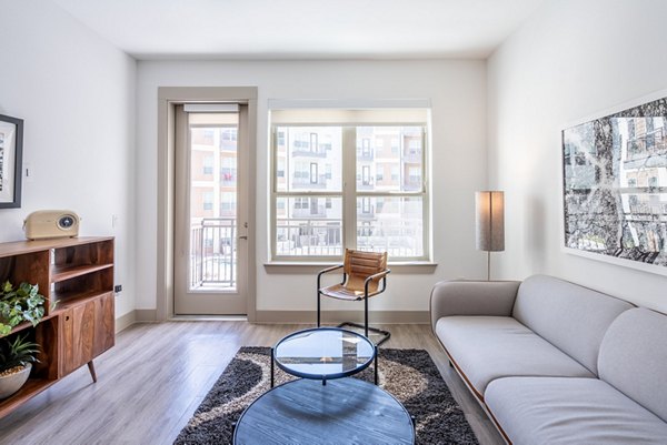 Contemporary living room with cozy seating and large windows at Alexan Braker Pointe Apartments