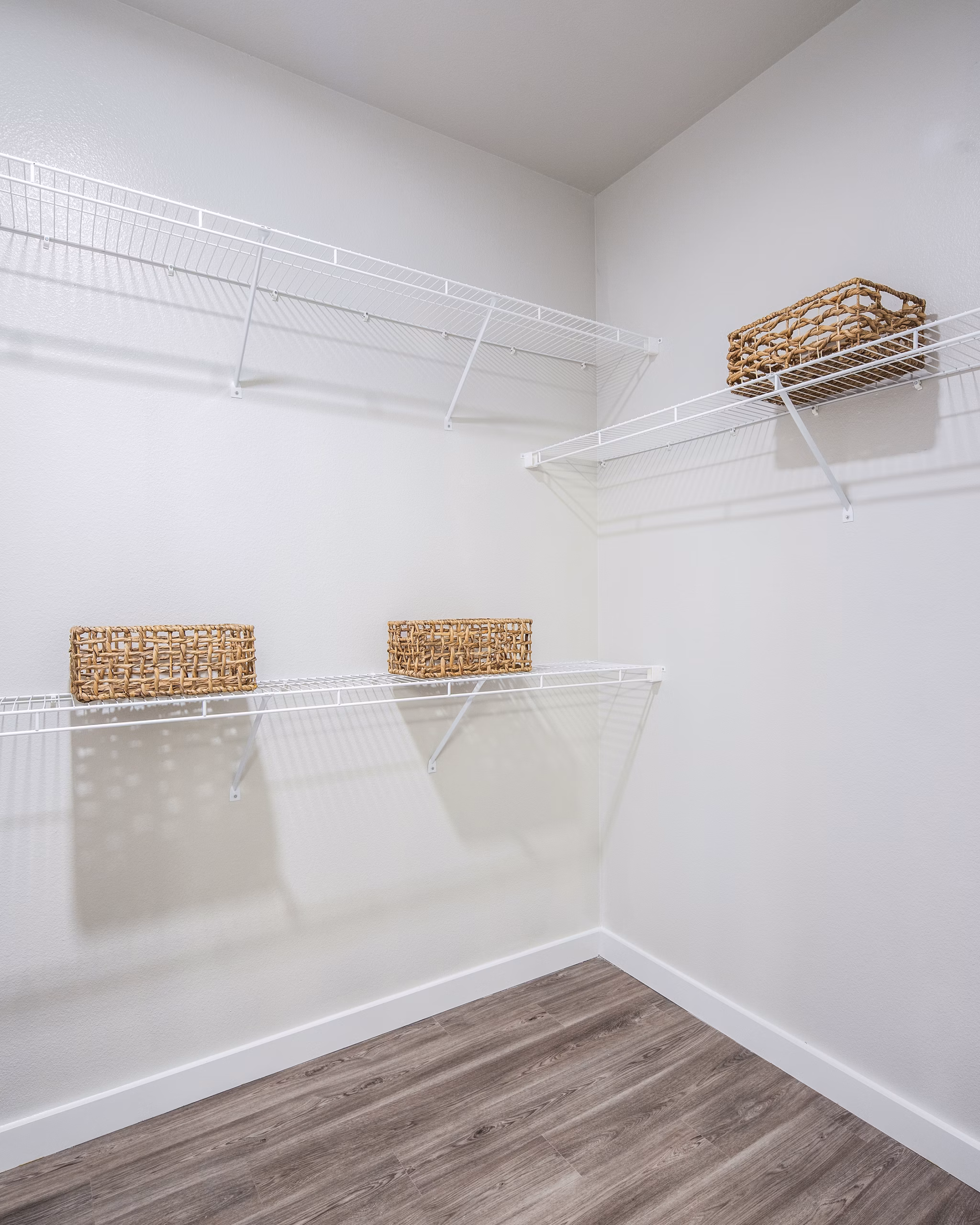Empty closet with white wire shelving and woven baskets in luxury apartment