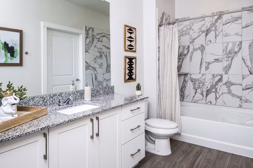 Modern bathroom featuring granite countertop and marble-patterned shower wall in luxury apartment
