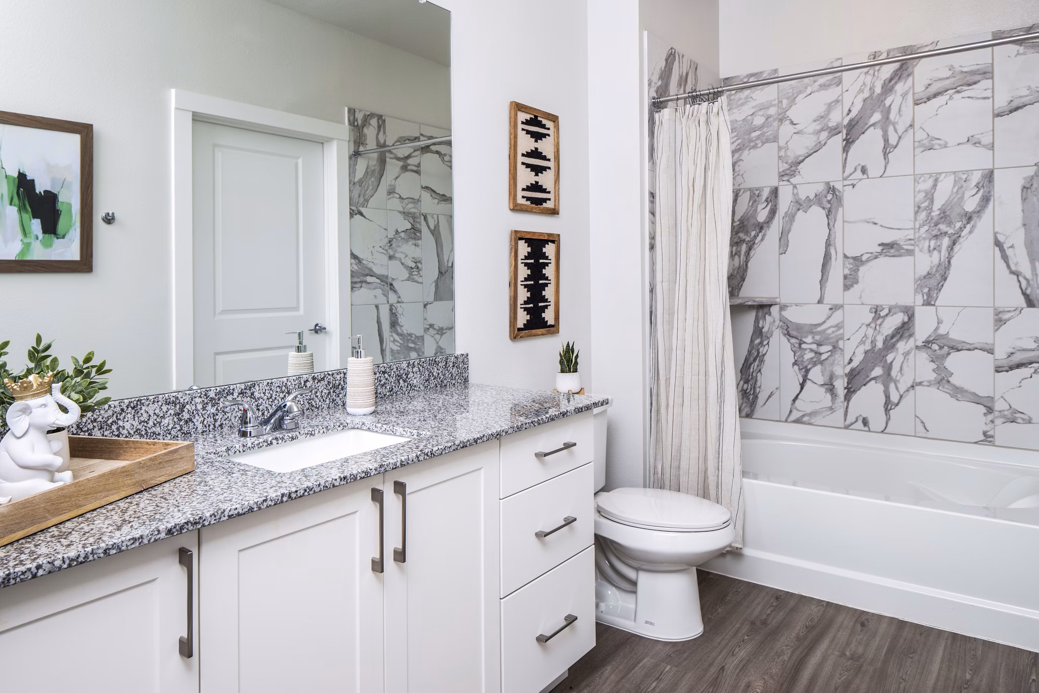Modern bathroom featuring granite countertop and marble-patterned shower wall in luxury apartment