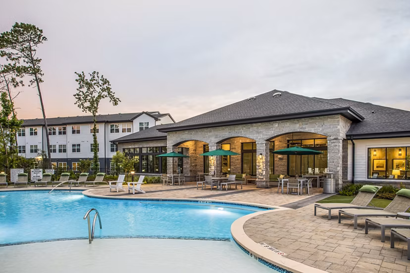 Resort-style swimming pool area with lounge chairs and modern apartments in the background