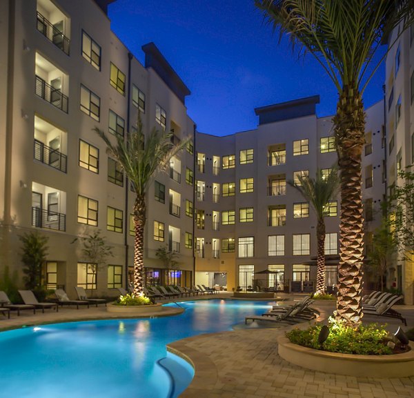 Resort-style pool at The Millennium Six Pines Apartments, featuring lush landscaping and spacious sundeck for relaxation and leisure activities