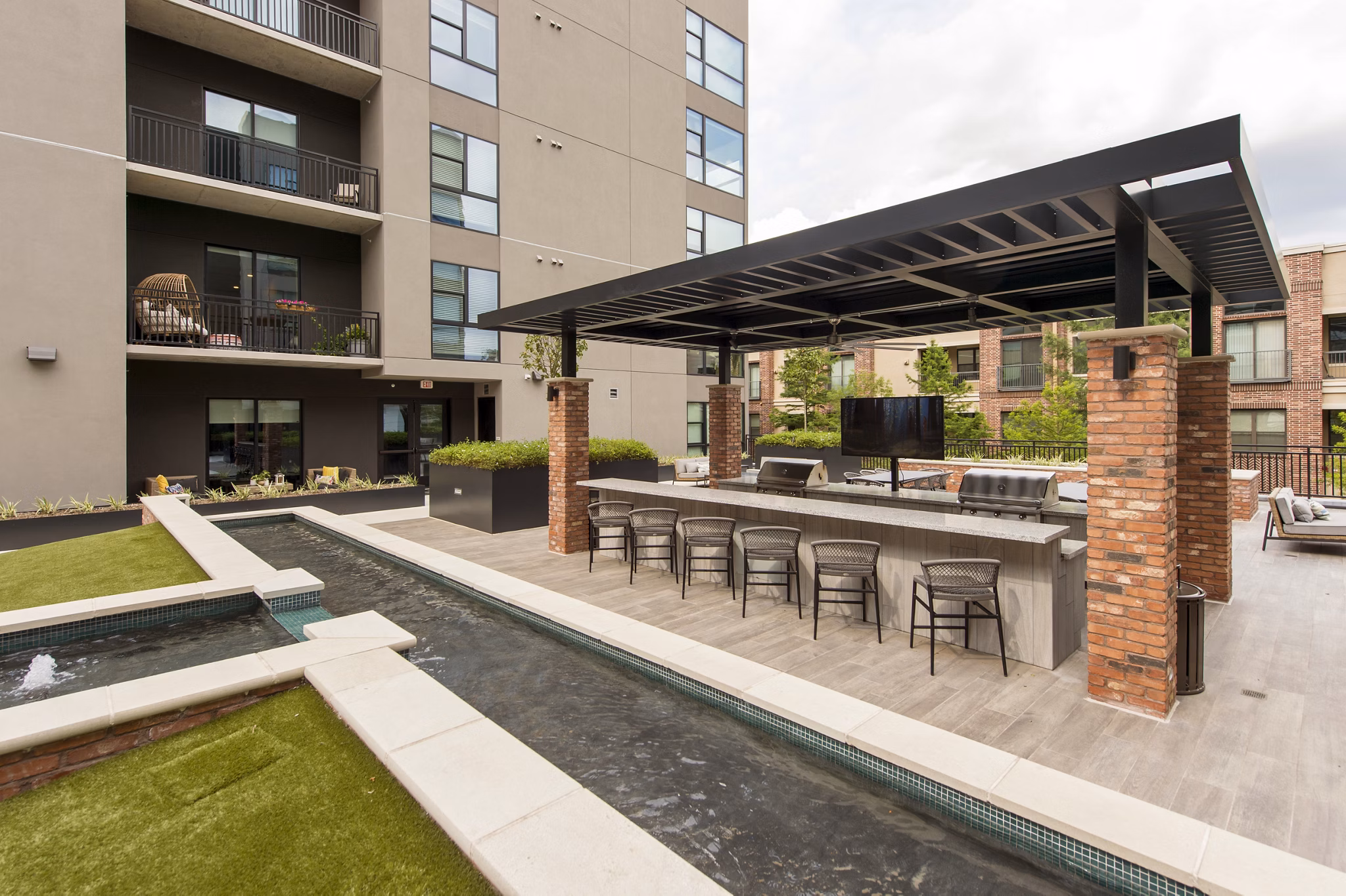 Outdoor grill area with modern seating at The Lane at Waterway Apartments in a lush setting