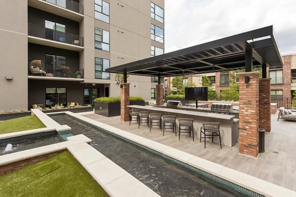 Outdoor grill area with modern seating at The Lane at Waterway Apartments in a lush setting