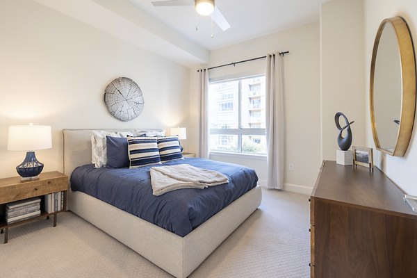 Cozy bedroom featuring a bed, nightstand, lamp, and dresser with natural light from a window
