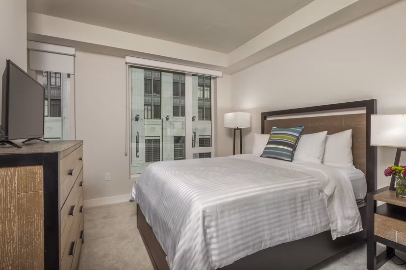 Elegant bedroom with modern decor at mResidences Olympic & Olive Apartments, featuring a cozy queen-size bed and stylish furnishings