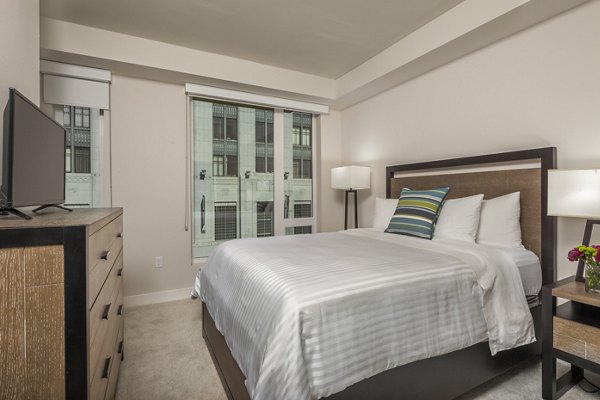 Elegant bedroom with modern decor at mResidences Olympic & Olive Apartments, featuring a cozy queen-size bed and stylish furnishings