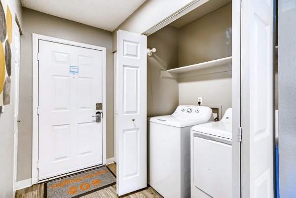 Laundry room with entrance to living room at Loretto Heights Apartments, offering convenience and luxury in open-concept design
