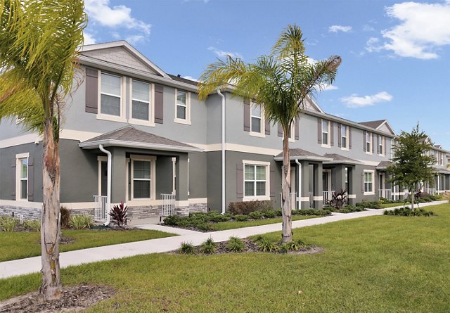 A row of modern townhouses with landscaped front yards and palm trees under a clear sky.