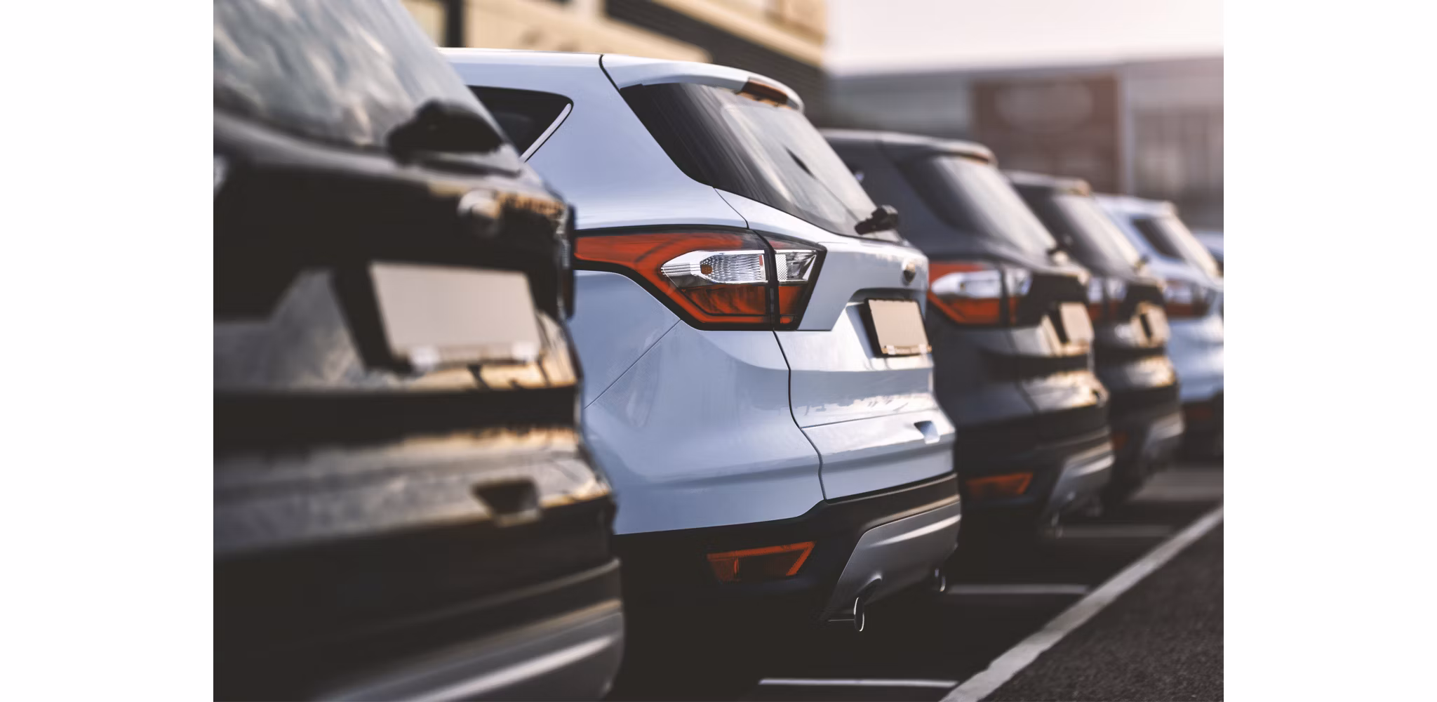 Diagonal view of a row of cars parked in a lot, highlighting the rear lights and designs of the vehicles.