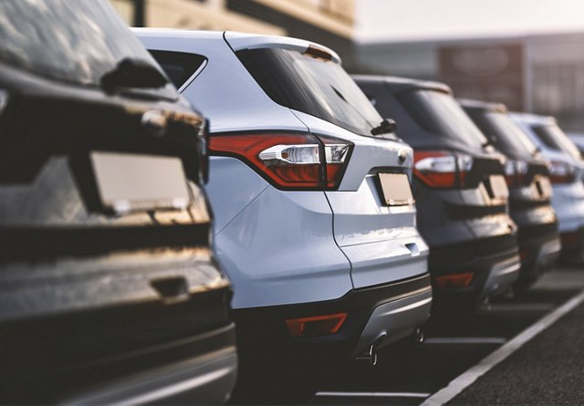 Diagonal view of a row of cars parked in a lot, highlighting the rear lights and designs of the vehicles.