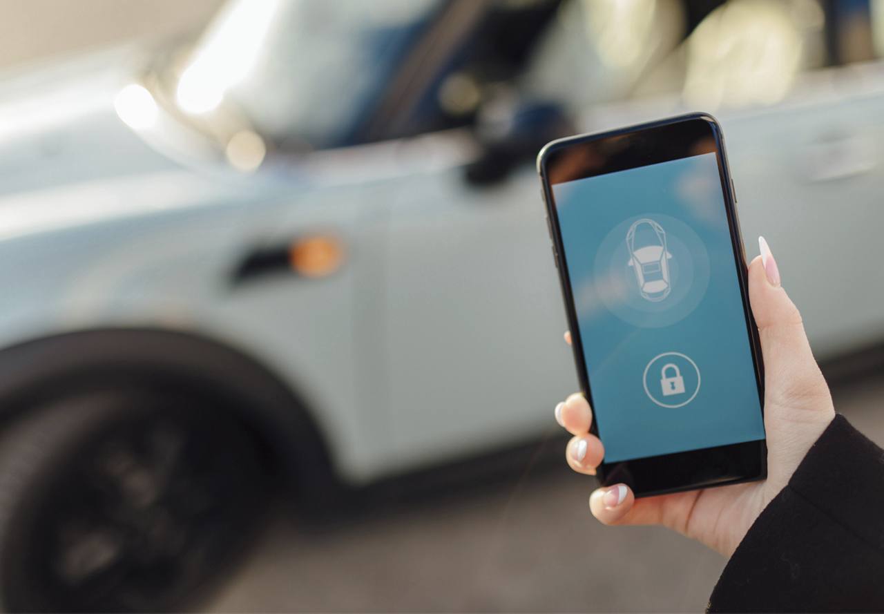 A hand holding a smartphone with a car security app on the screen, with a blurred car in the background.