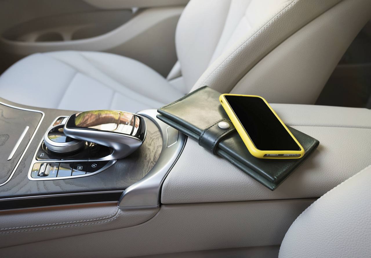 A smartphone on top of a wallet, placed on the center console inside a car, with the gear shift nearby.