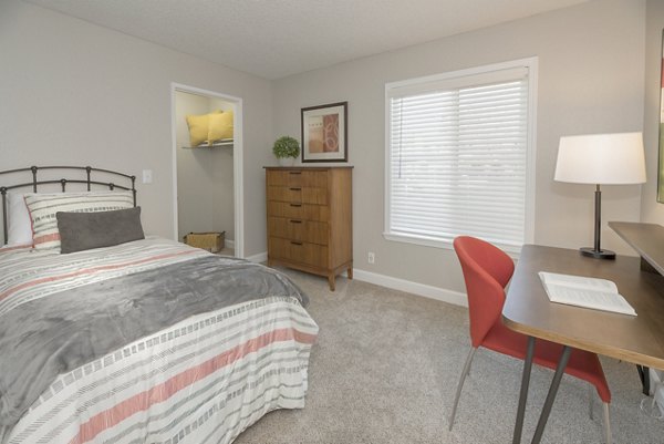Cozy bedroom with plush bedding and large window at The Hills Apartments