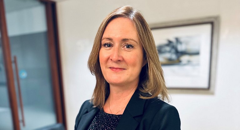 Portrait of a professional woman with long hair in business attire standing in an office.