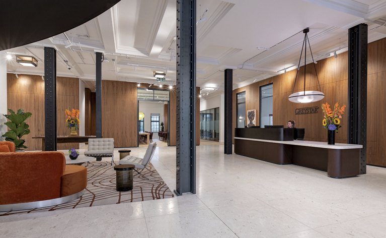 The Greystar corporate office in London features a welcoming lobby adorned with warm accents and stylish decor, creating an inviting atmosphere for guests as they enter the building.