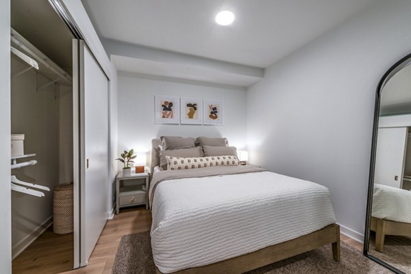 Cozy bedroom featuring a bed, nightstand, artwork, mirror, and open closet in luxury apartment