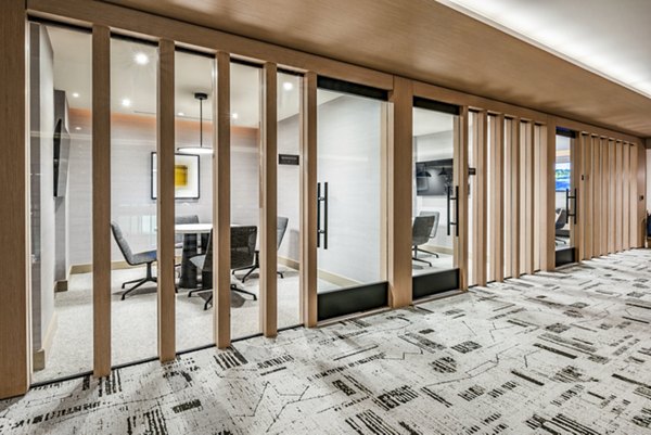 Modern office space featuring glass-walled meeting rooms and a patterned carpeted hallway in luxury apartment community