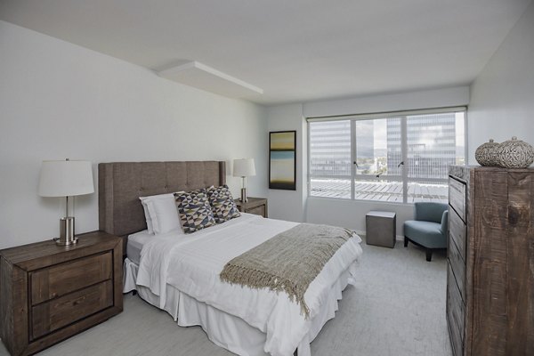 Bright bedroom with large window, wooden furniture, and neutral decor at The View Apartments