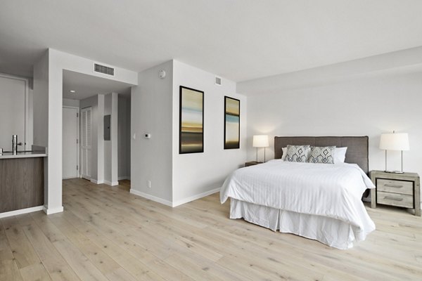 Minimalist bedroom with wooden floor, white bedding, and artwork at The View Apartments