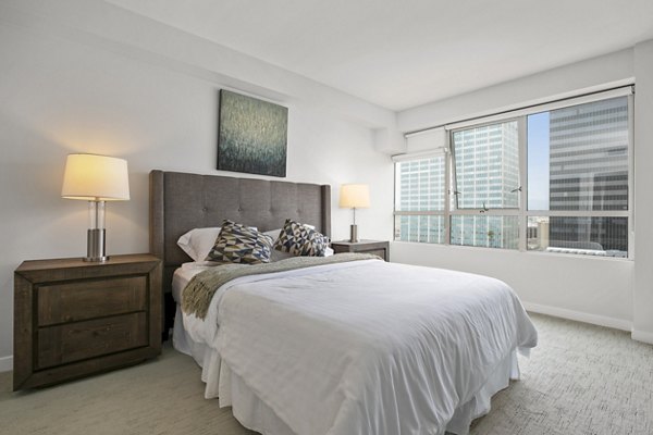 Bright bedroom with large window, bed, nightstands, and lamps at The View Apartments