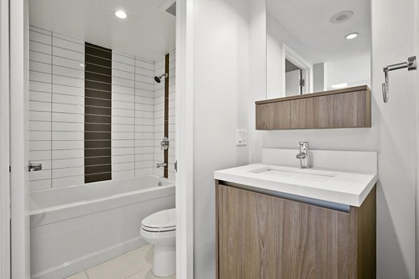 Sleek bathroom with wood vanity, white tiles, and bathtub at The View Apartments