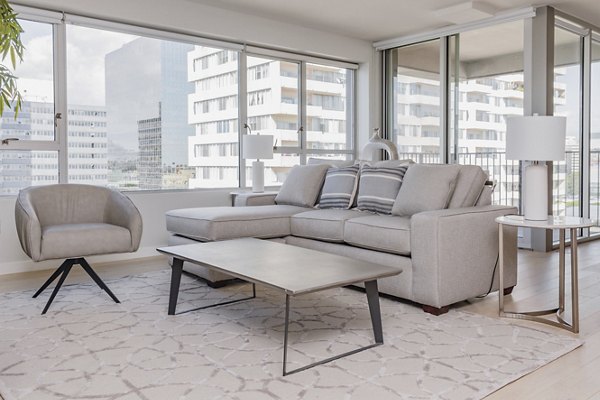 Bright living room with gray furniture and large windows at The View Apartments