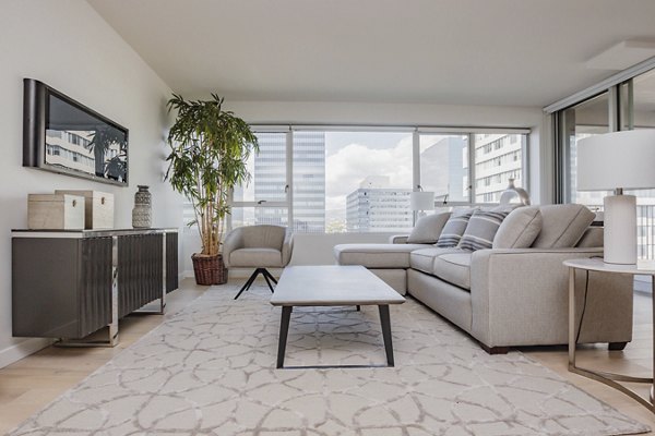 Bright living room with large windows, neutral furniture, and plants at The View Apartments