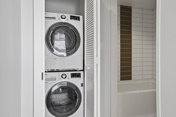 Compact laundry area with stacked washer and dryer next to a sleek tiled bathtub at The View Apartments luxury apartments