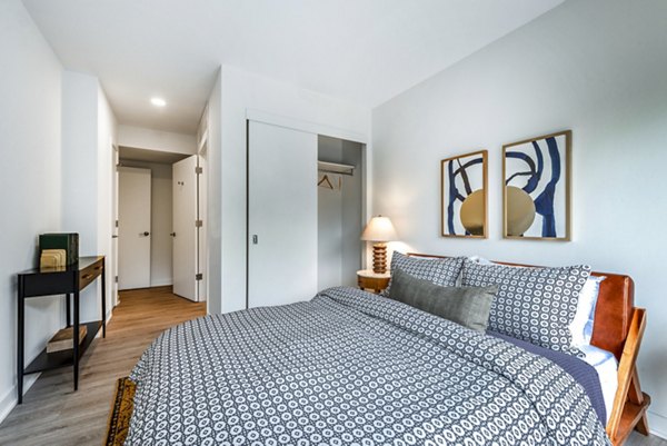 Cozy bedroom featuring patterned bedding, abstract wall art, and a stylish lamp at luxury apartments