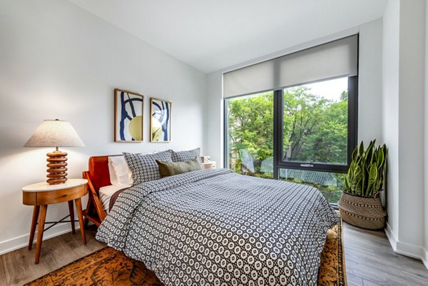Cozy bedroom with patterned bedding, lamp, wall art, and tree views through the window