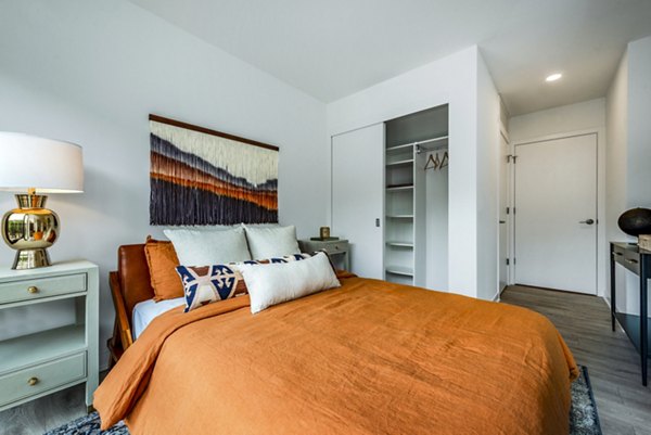 Cozy bedroom with orange bedding, a lamp, and artwork, featuring an open closet in luxury apartments