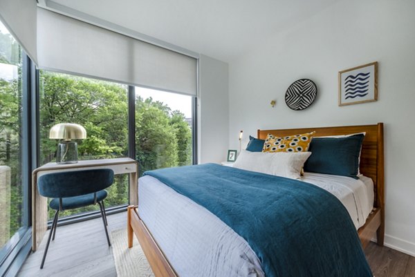Modern bedroom with a bed, desk, and large window in luxury apartments