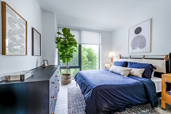 Modern bedroom featuring a bed, dresser, potted plant, and stylish wall art in luxury apartments