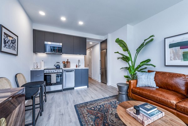 Modern living room and kitchen with leather sofa, wooden coffee table, and dark cabinets in luxury apartment