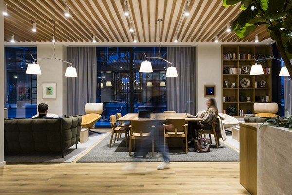 Modern and stylish common area at Bloom East Apartments in London, featuring comfortable seating, a wooden ceiling, bookshelves, and warm lighting.