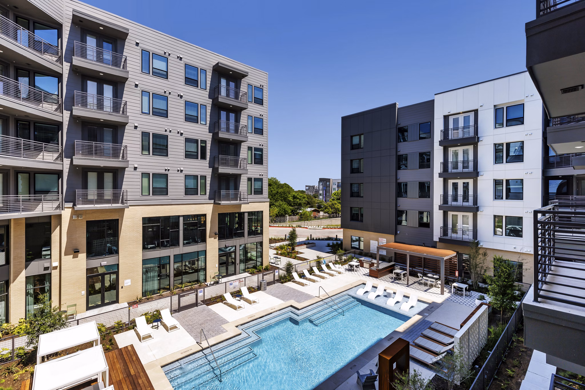 Community swimming pool at Crosstown Apartments with sun loungers and greenery Enjoy leisure and relaxation in a premium urban setting