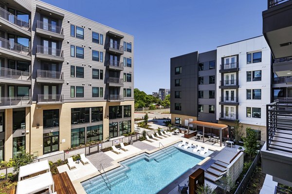 Community swimming pool at Crosstown Apartments with sun loungers and greenery Enjoy leisure and relaxation in a premium urban setting
