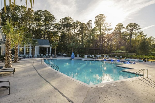 Pool at Riverwood Apartments with modern lounge chairs and surrounded by lush landscaping