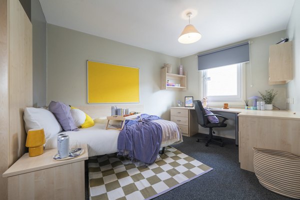 Interior shot of a Canvas The Heights apartment in Birmingham, showcasing a bright and cozy bedroom with a study desk, vibrant yellow accents, and modern furnishings.