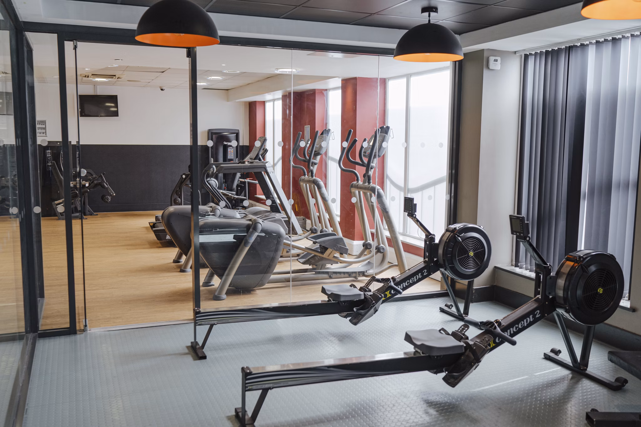 Fitness room at Canvas The Heights apartments, featuring modern workout equipment, rowing machines, treadmills, and large windows providing natural light.