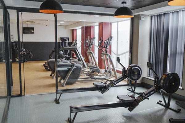 Fitness room at Canvas The Heights apartments, featuring modern workout equipment, rowing machines, treadmills, and large windows providing natural light.