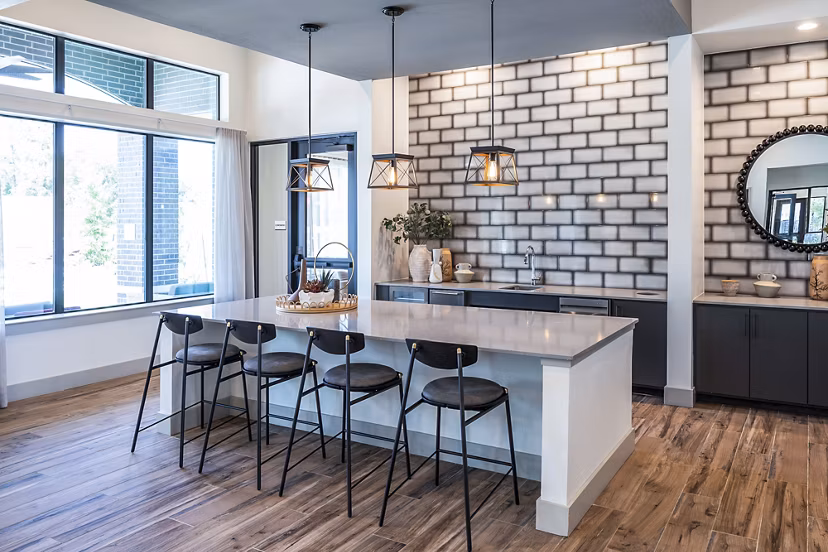 Modern kitchen featuring a large island, bar stools, and pendant lights with a brick-patterned backsplash in luxury apartments