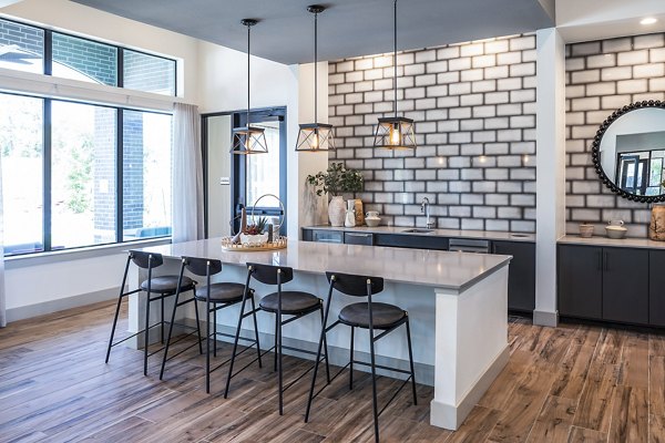 Modern kitchen featuring a large island, bar stools, and pendant lights with a brick-patterned backsplash in luxury apartments
