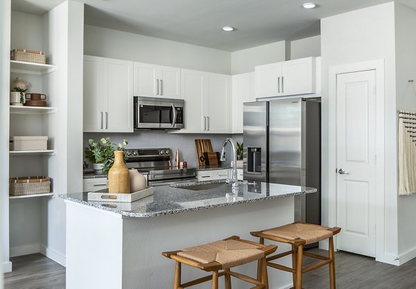 Modern kitchen featuring white cabinets and stainless steel appliances in luxury apartments, with a granite countertop island and wooden stools
