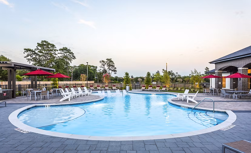 Inviting outdoor swimming pool area with lounge chairs and red umbrella tables at luxury apartments