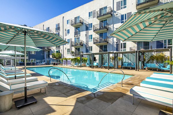 Refreshing outdoor pool at Aliso Apartments, featuring lounge chairs and lush greenery, perfect for relaxation and enjoyment