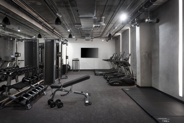 Modern fitness center with weight machines and treadmills at The Charlie WeHo Apartments